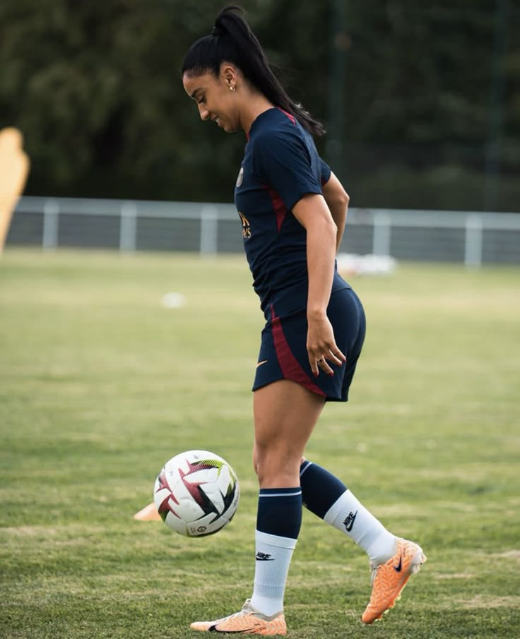 a woman kicking a soccer ball on top of a field