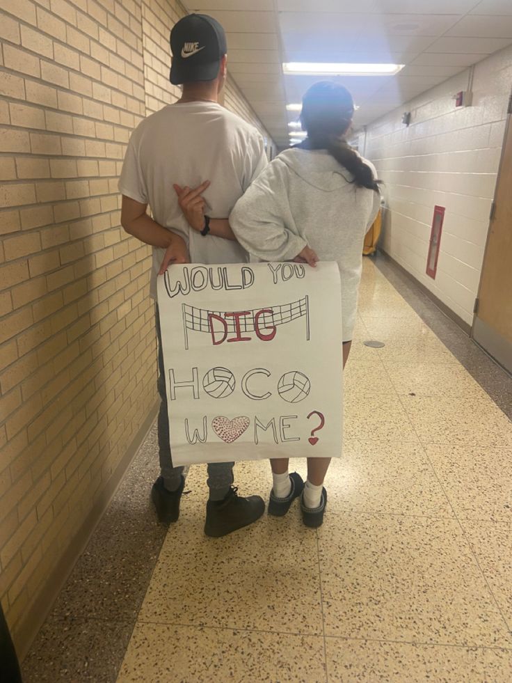 a man and woman standing next to each other in a hallway holding a sign that says, would you dig hsc home?