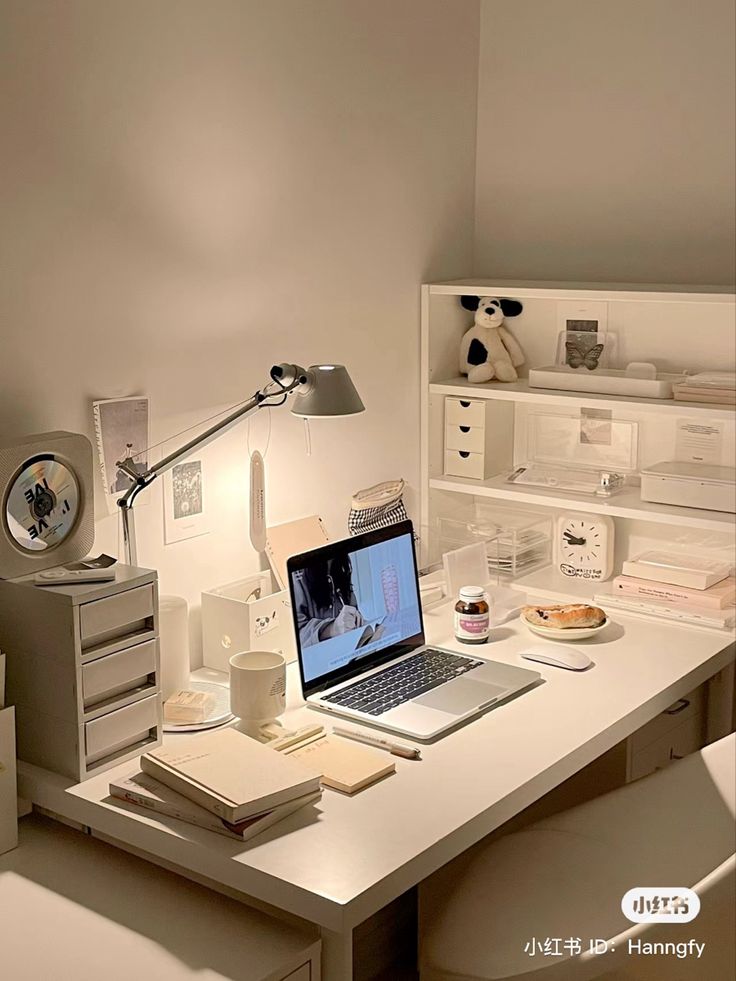 a laptop computer sitting on top of a white desk next to a lamp and books