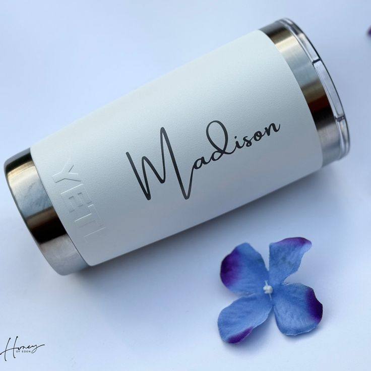 a bottle with the word madison written on it next to blue and purple flower petals