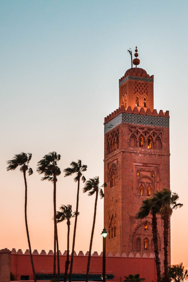 a tall tower with a clock at the top and palm trees in front of it