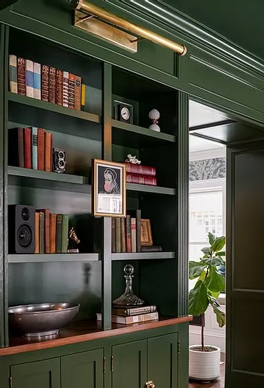 the bookshelves are green and there is a bowl on the table in front of them