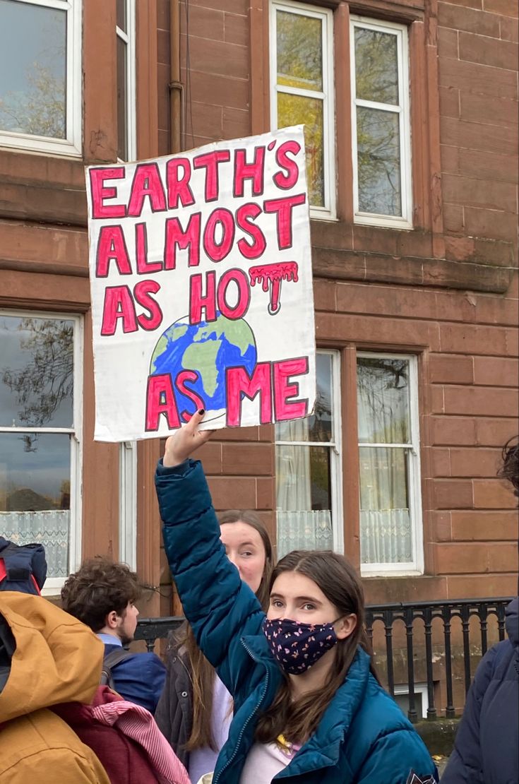 a woman holding up a sign that says earth's almost as hot as me