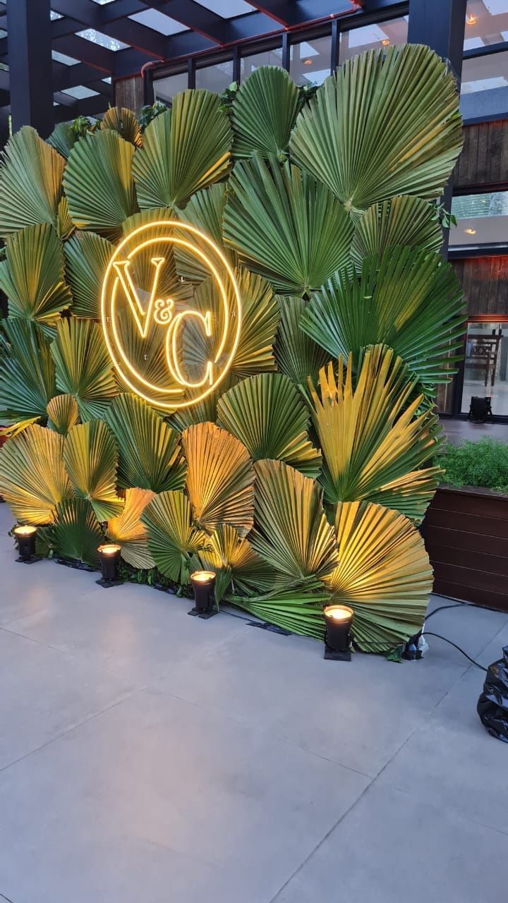 the neon sign is lit up in front of palm leaves and lights that are attached to the wall