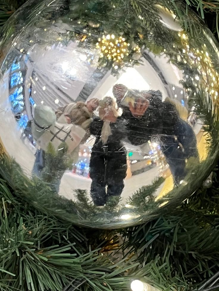 an ornament hanging from a christmas tree with people reflected in the glass ball