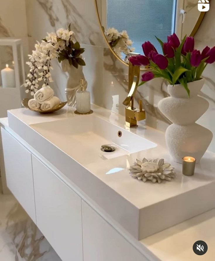 a white bathroom with flowers and candles on the sink counter next to it is decorated in gold