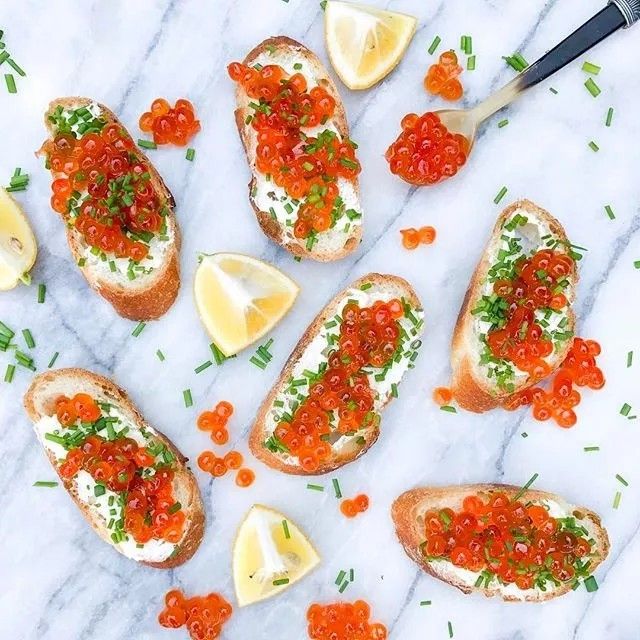 several pieces of bread topped with red cavias and lemon wedges on a marble surface