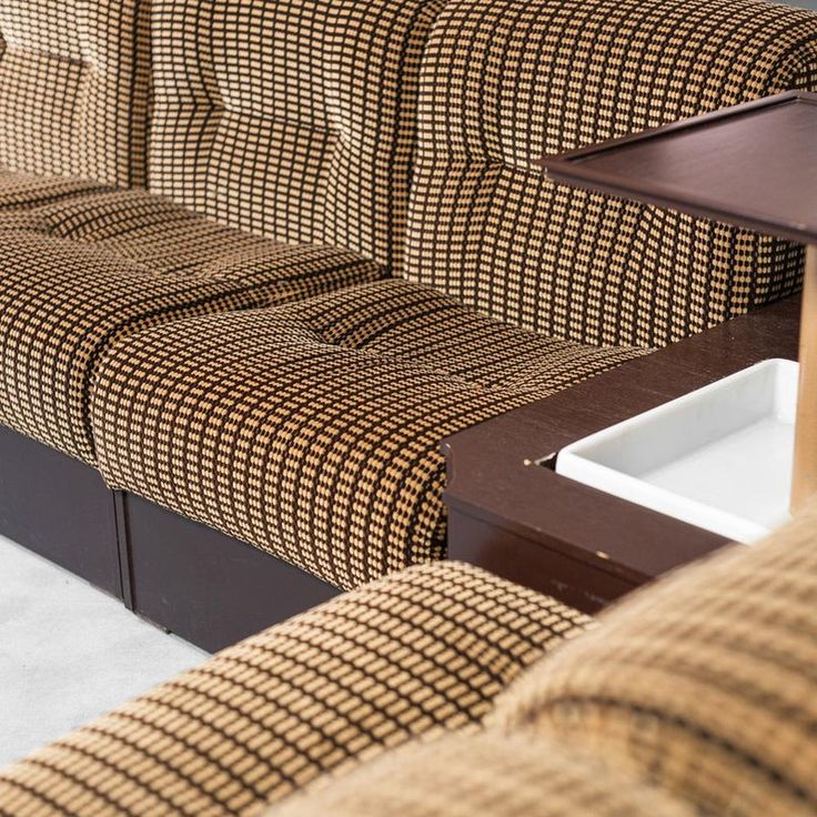 a brown and white checkered couch sitting next to a wooden table on top of a carpeted floor