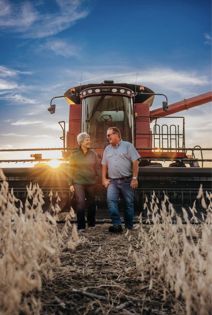 two people standing in front of a combine truck at sunset with the sun behind them