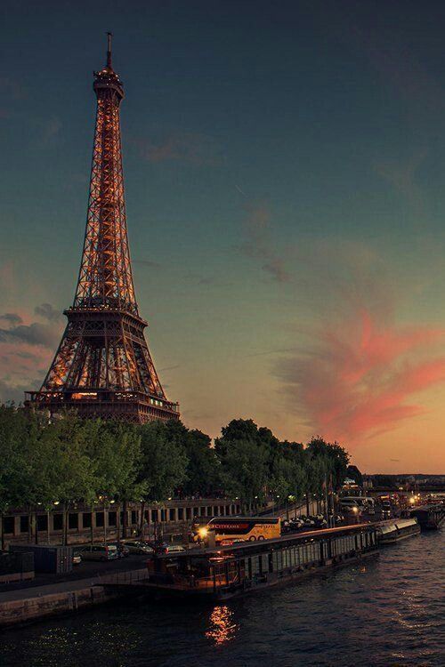 the eiffel tower lit up at night with pink clouds in the sky behind it