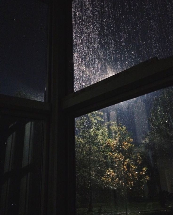 an open window at night with rain falling on the windows and trees in the background