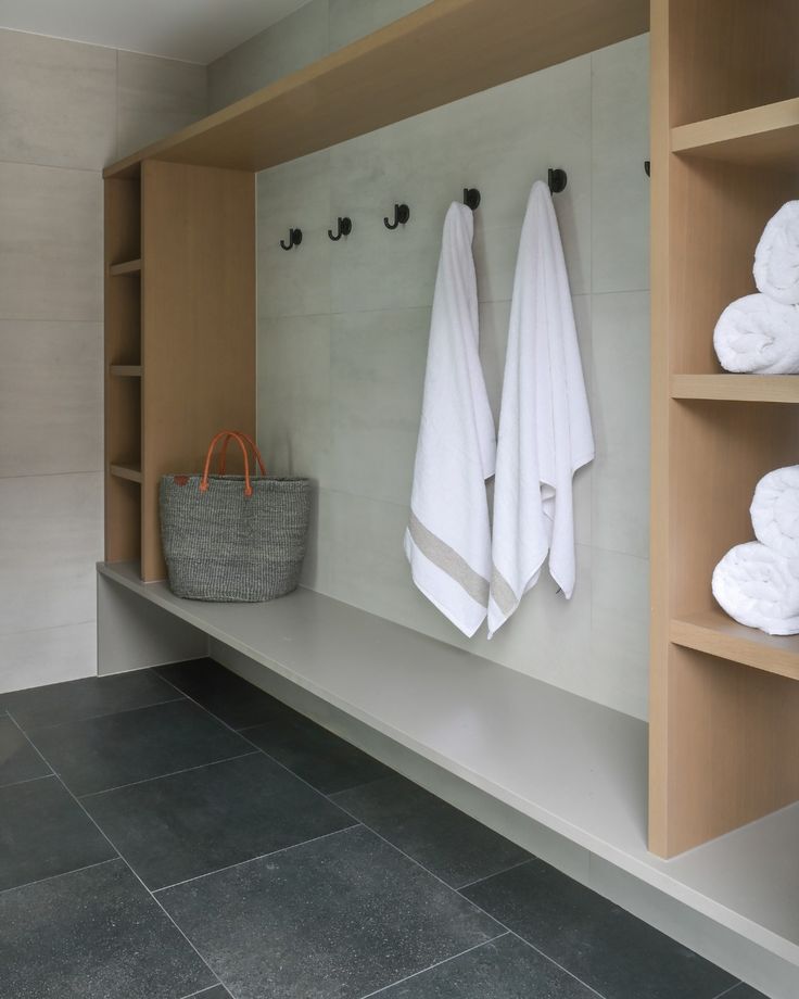 towels are hanging on the wall next to some shelves and baskets in a room with gray tile flooring