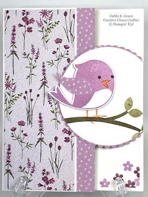 a card with a bird sitting on a branch in front of purple and white flowers