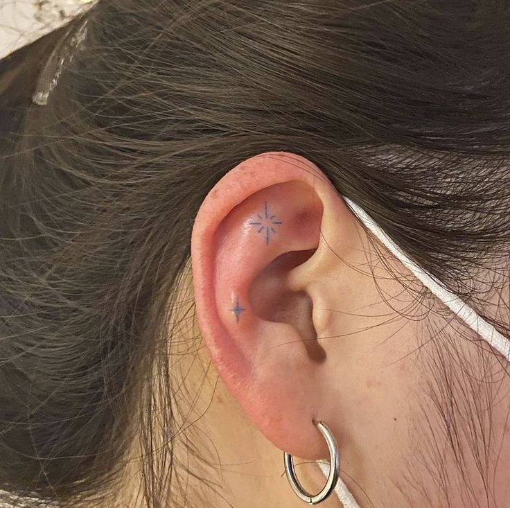 a woman's ear has a small star tattoo on it, and is wearing a pair of silver hoop earrings