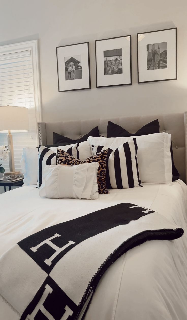 a white bed with black and white pillows in a bedroom next to two pictures on the wall