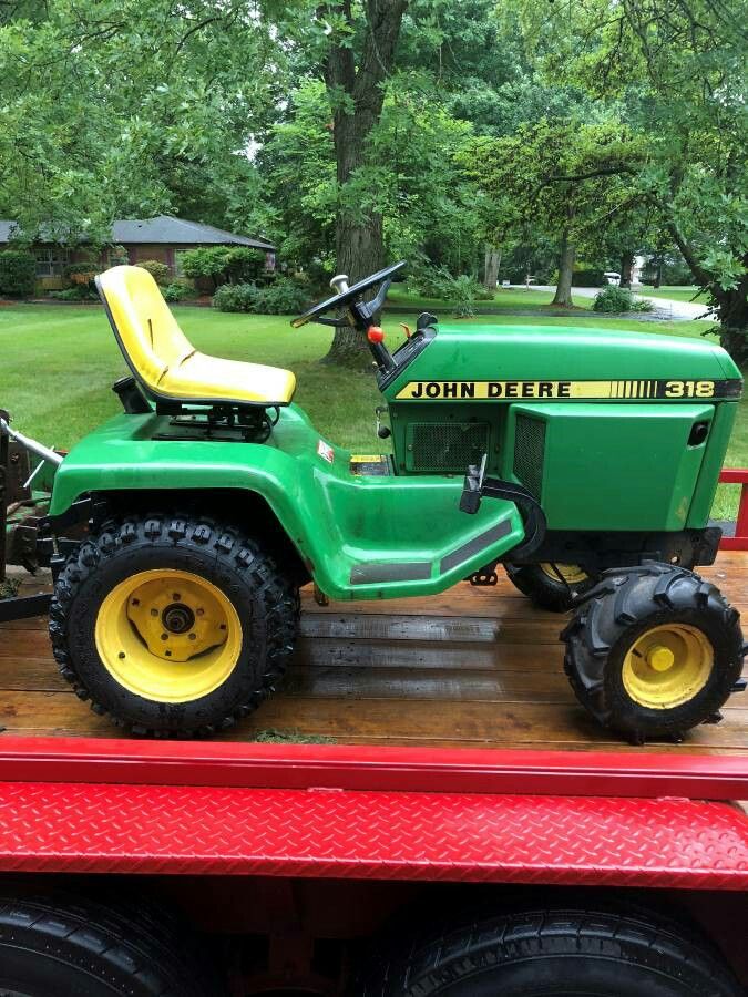 a green tractor sitting on the back of a red trailer in front of some trees