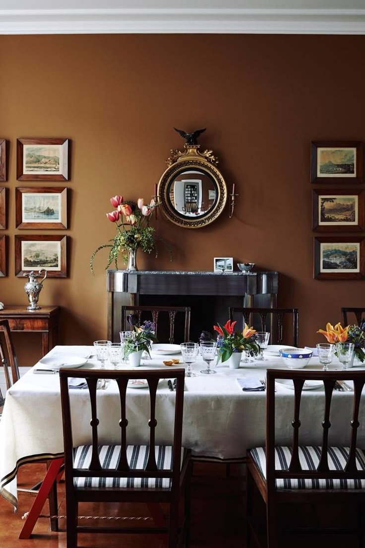 a dining room table is set with place settings and flowers on the table, along with several framed pictures