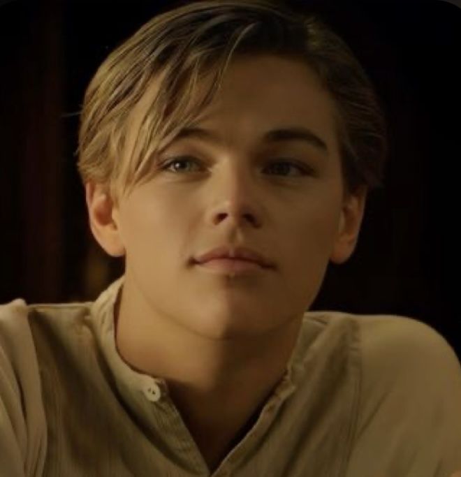 a young man with blonde hair wearing a tan shirt and looking at the camera while sitting down