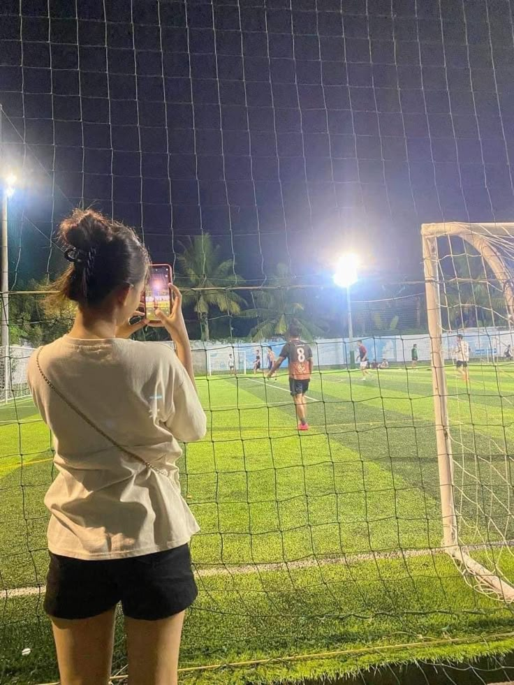 a woman standing in front of a soccer goal taking a photo with her cell phone