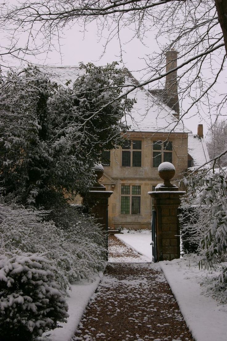 a snow covered path leading to a large house with trees and bushes on either side