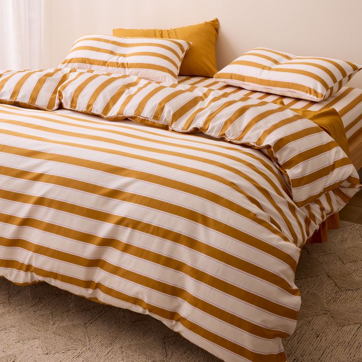 an orange and white striped comforter on a bed with two pillows in the corner