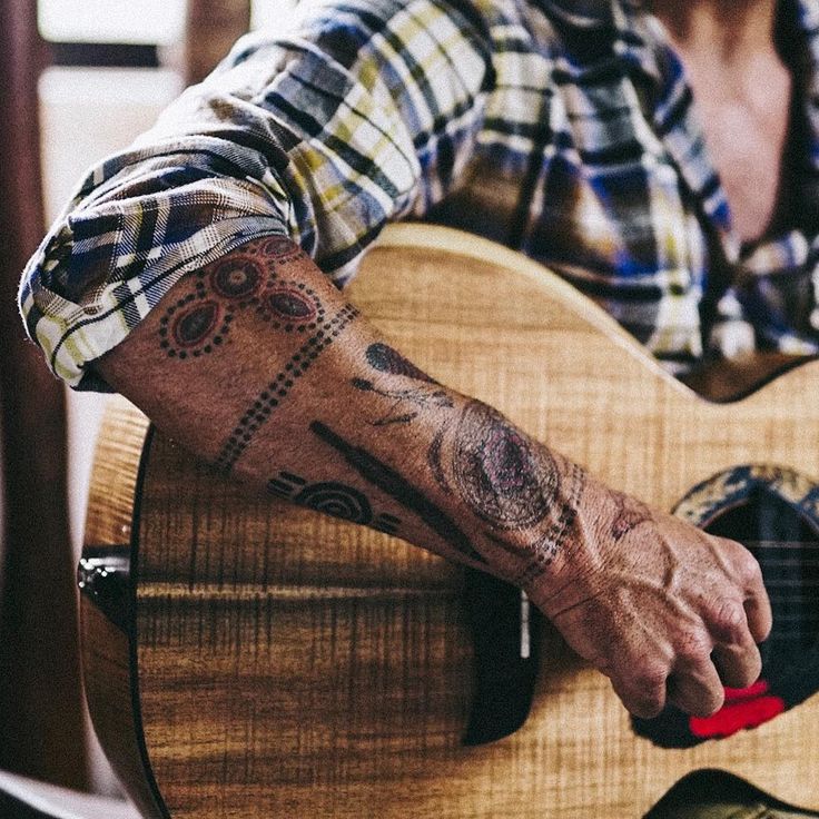 a man with a tattoo on his arm is playing an acoustic guitar while wearing a plaid shirt