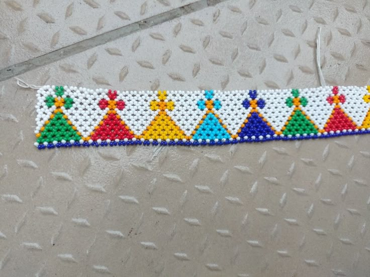 a white beaded bracelet with colorful designs on it's side and an arrow in the middle