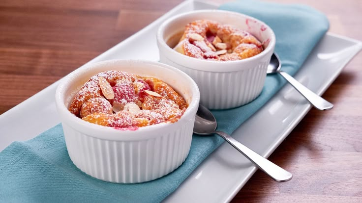 two desserts sitting on top of a white plate next to spoons and forks