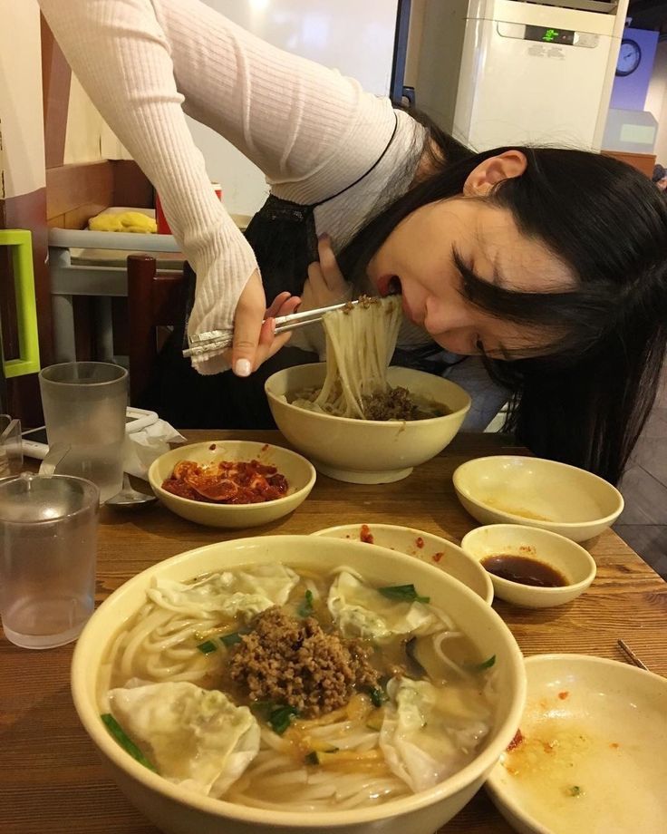 a woman is eating noodles with chopsticks at a table