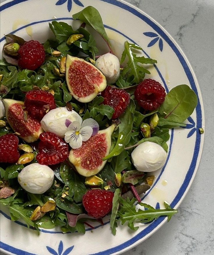 a salad with figs, strawberries and spinach on a blue and white plate