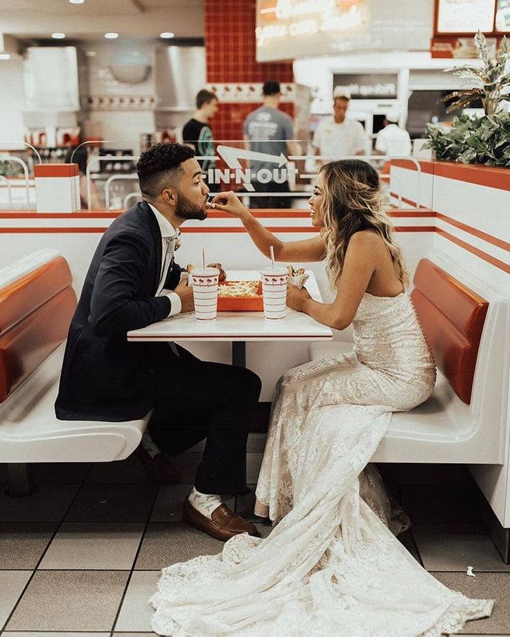 a man and woman sitting at a table in a fast food restaurant feeding each other