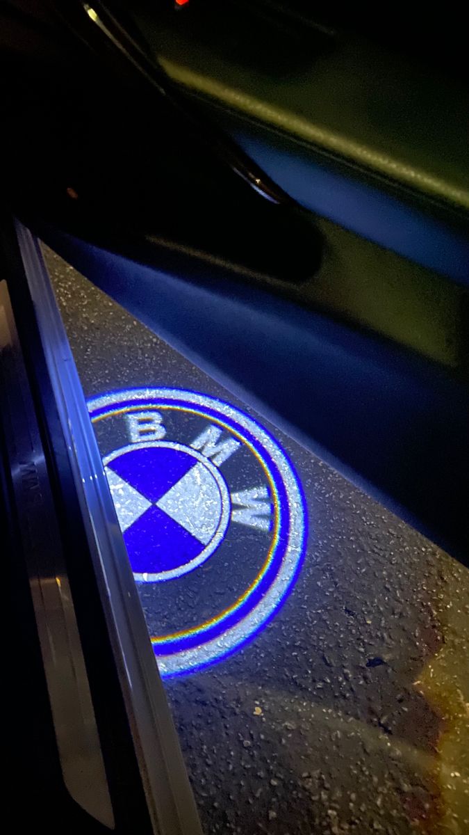 the bmw logo is shown on the floor in front of a car window at night