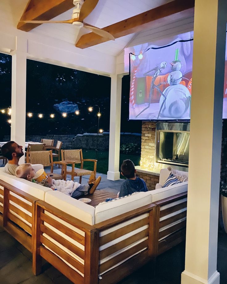 people sitting on couches in front of a large screen tv at the back of a house