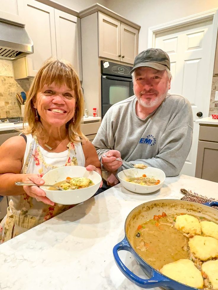 two people sitting at a kitchen table with plates of food