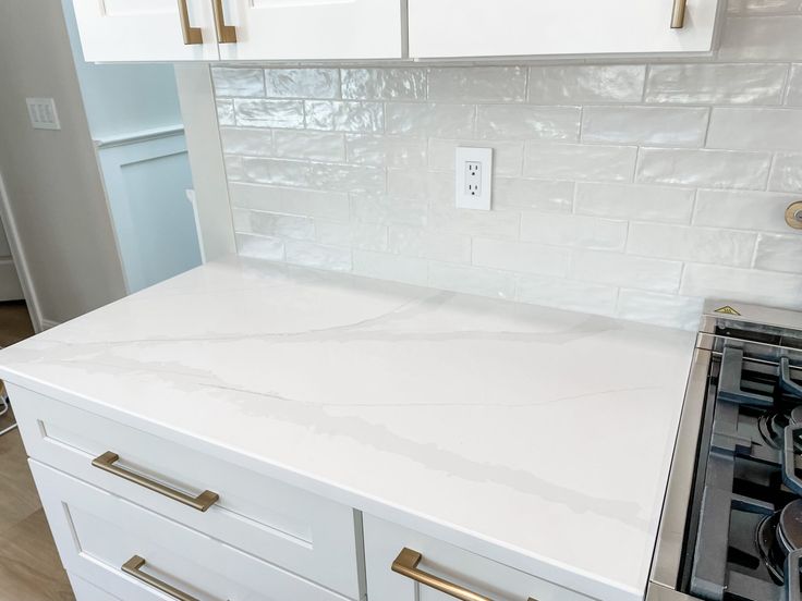 a kitchen with white cabinets and marble counter tops, gold pulls on the knobs