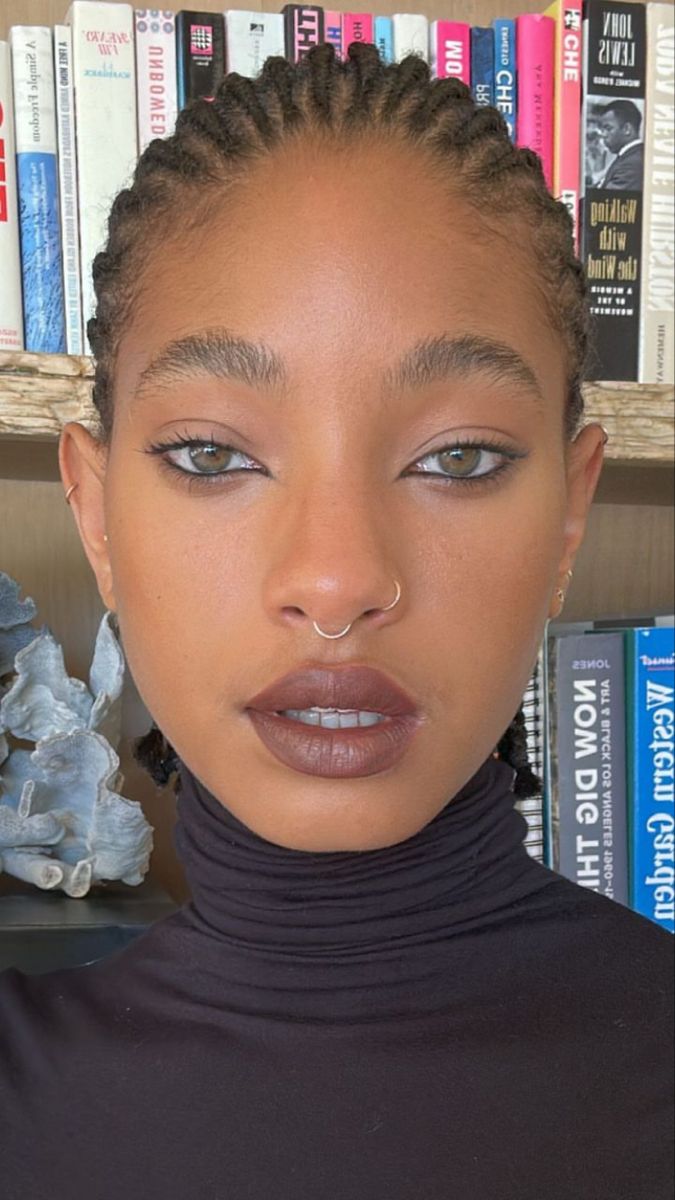 a woman with braids on her head standing in front of bookshelves and looking at the camera