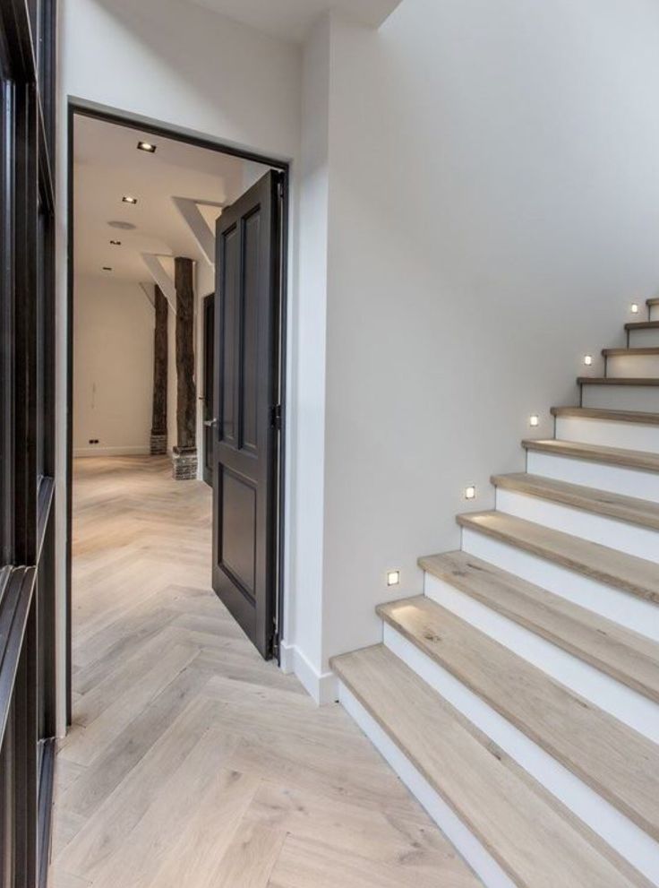 an open door leading to a white staircase with wooden handrails and light wood flooring