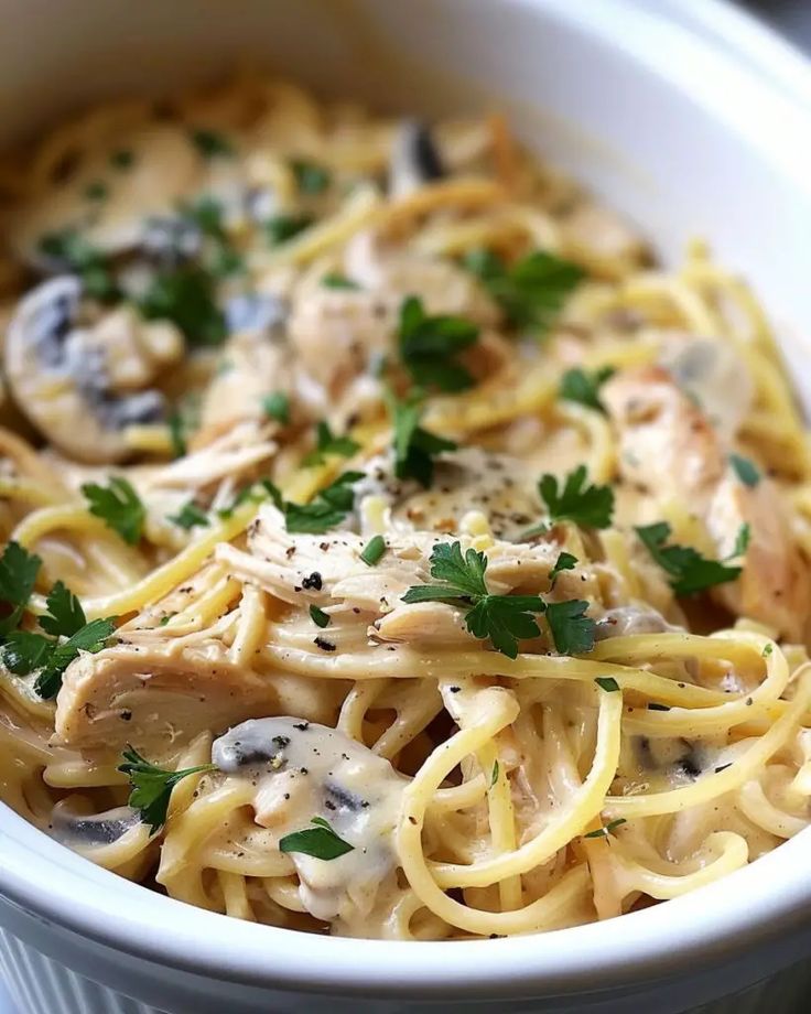 a white bowl filled with pasta covered in mushrooms and parsley on top of a table