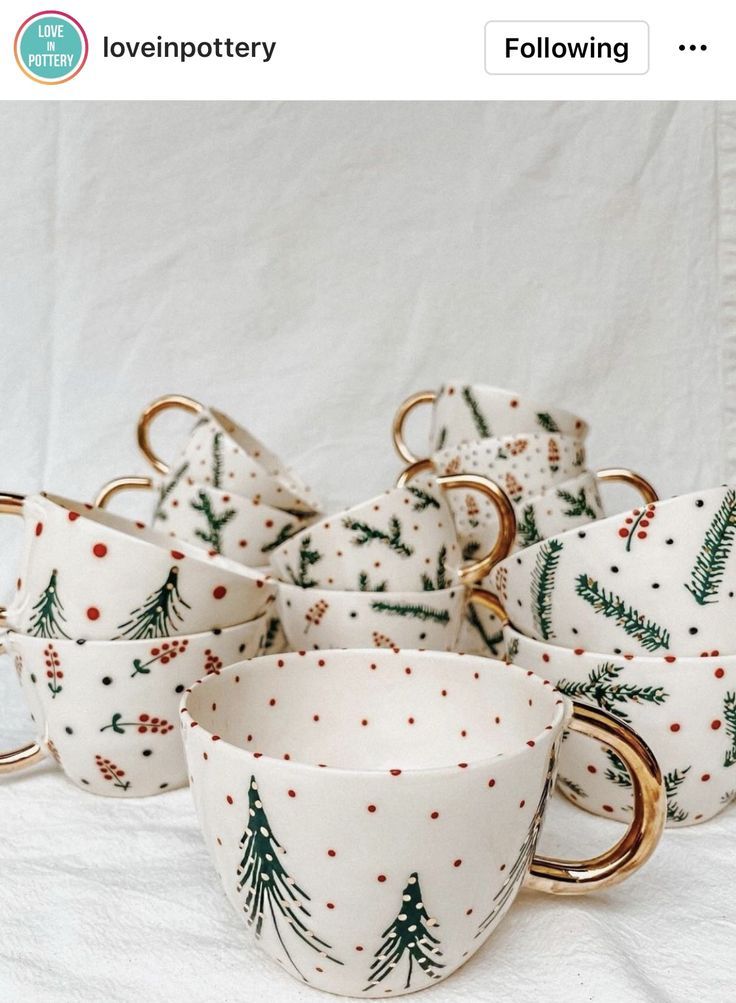 christmas themed coffee cups and saucers with gold rims on white background, surrounded by pine trees