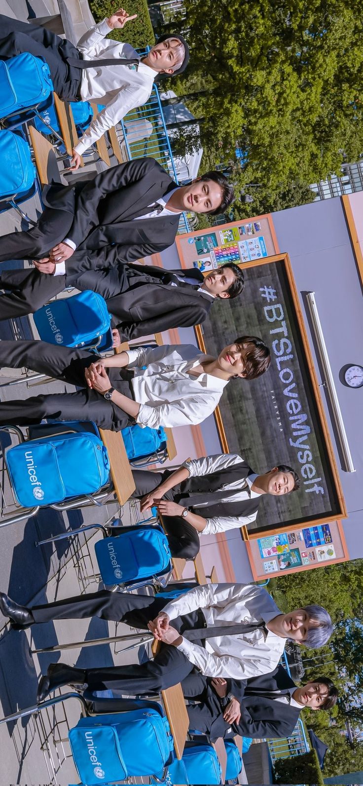 several people standing in front of a building with blue bags on their shoulders and one person holding a cell phone