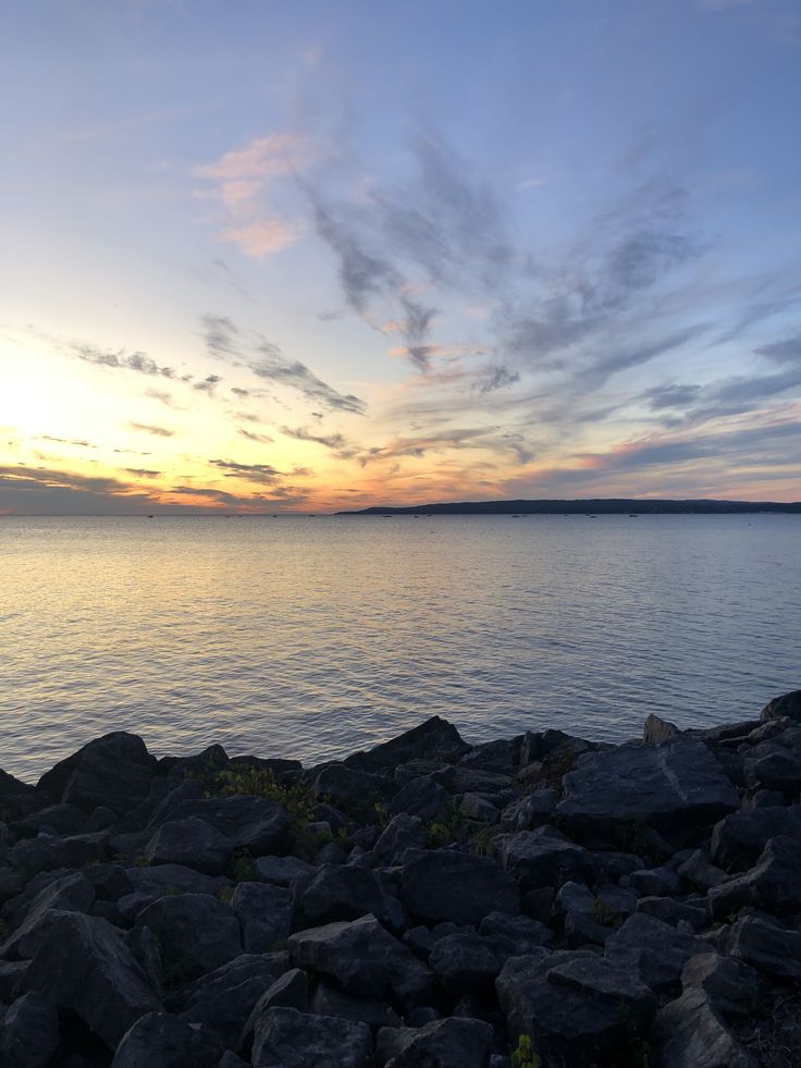 the sun is setting over the water and rocks