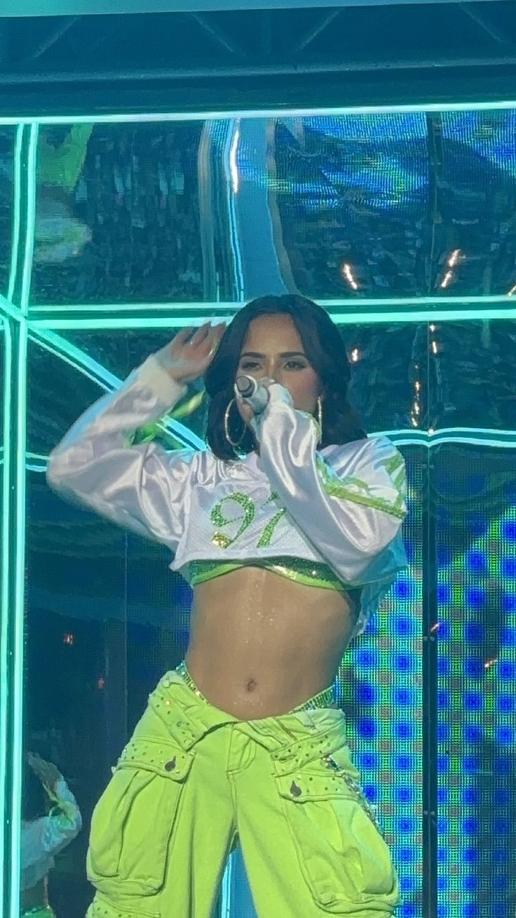 a woman in neon green pants and cropped top on stage with her hands behind her head