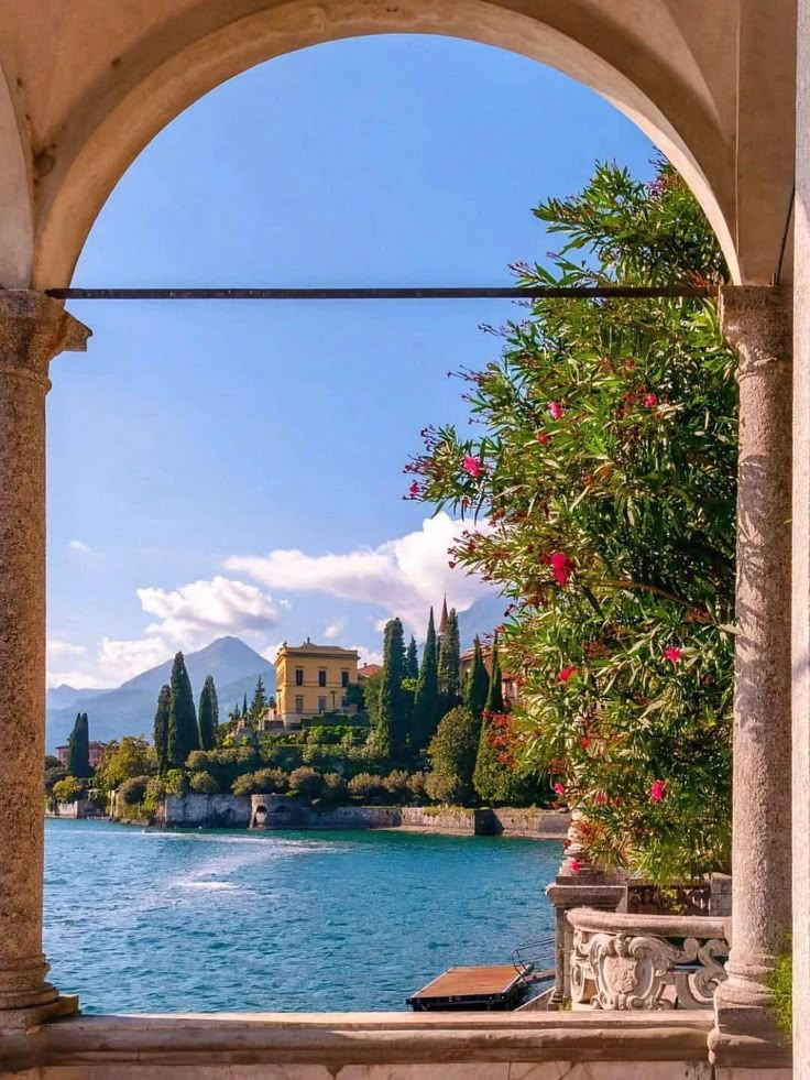 an archway leading to a lake with trees and buildings in the background