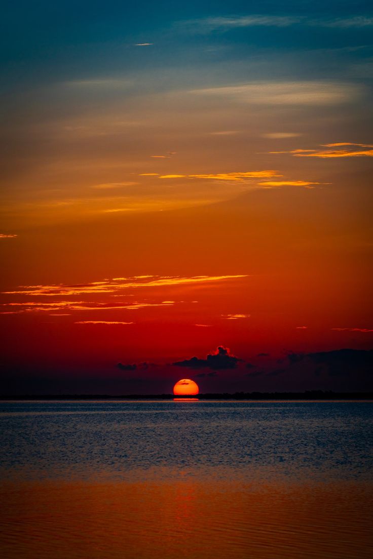 the sun is setting over the ocean with clouds in the sky and water below it