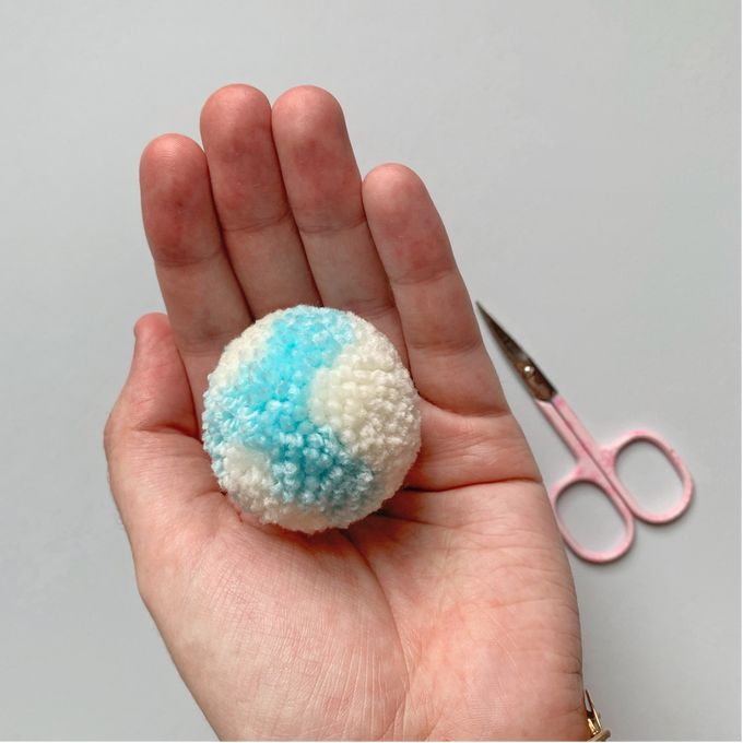 a hand holding a small blue and white object next to a pair of pink scissors