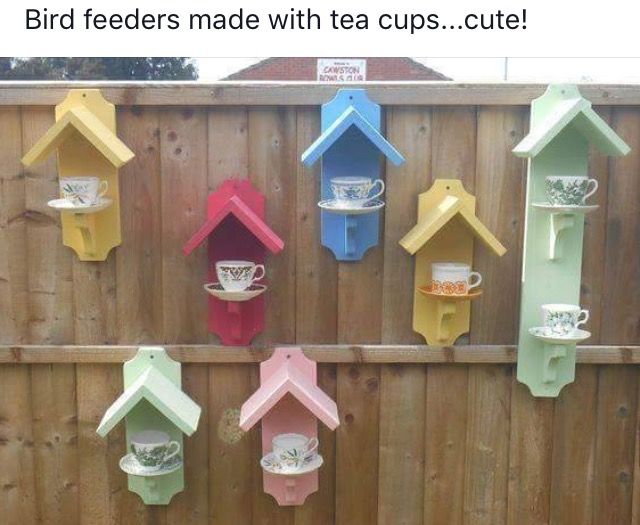 colorful birdhouses are hanging on the fence in front of a teacup cup and saucer holder