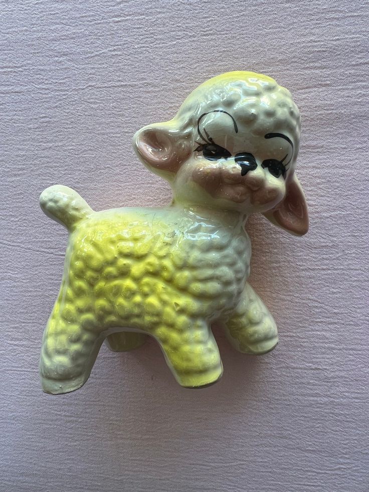 a yellow and white ceramic sheep ornament on a pink wall with black eyes