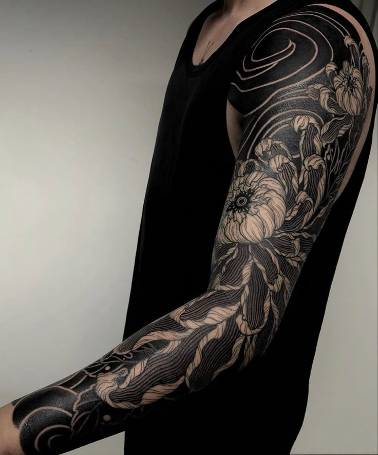 a man's arm covered in black and white tattoos with flowers on the arm