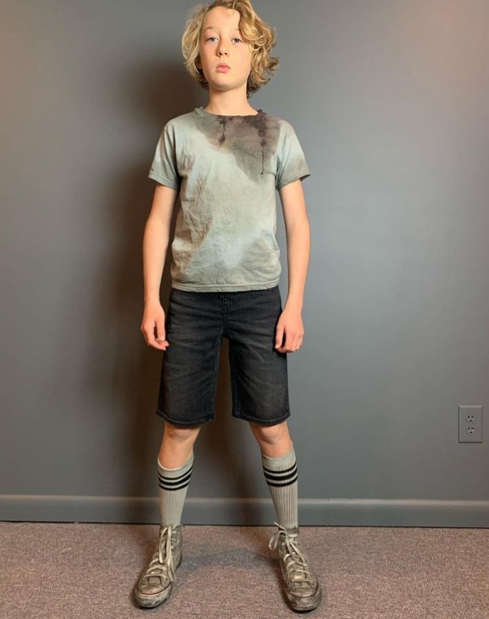 a young boy standing in front of a gray wall