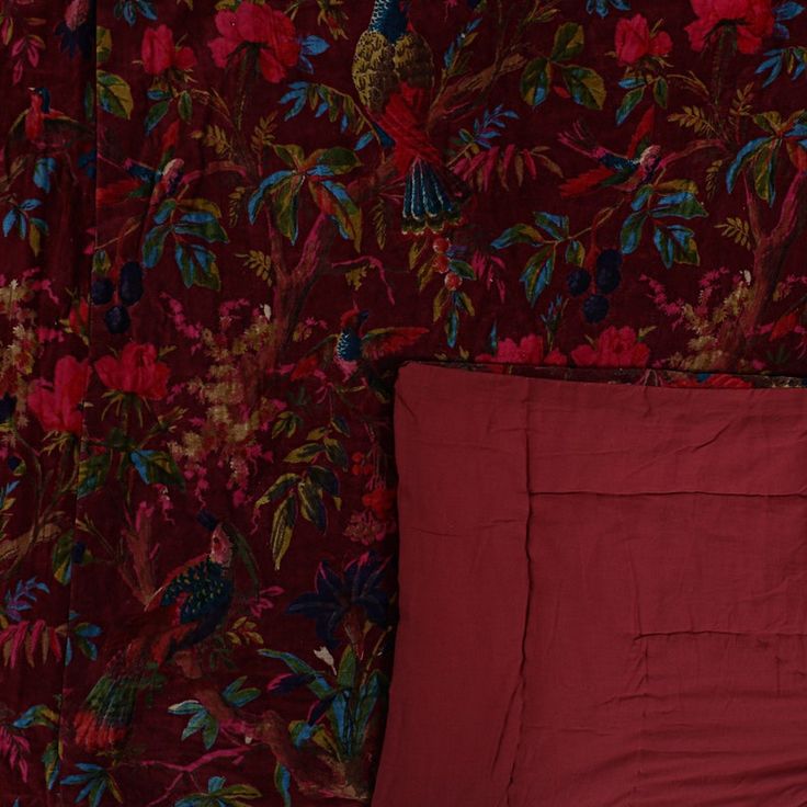 a red pillow sitting on top of a bed next to a wall covered in flowers